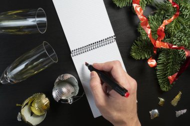 Genç bir adam, ahşap bir masanın üzerine deftere bir plan yazıyor.