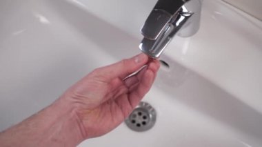 Temizlikten sonra parlak banyo musluğunun lastik contasıyla filtrenin kurulumu ve teftişi. Beyaz, temiz lavabo. Tesisat bakımı. Çilingir parçayı kuruyor ve suyu açıyor.