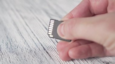 Genç bir adam elinde bir mikro Sd hafıza kartı tutuyor beyaz desenli ahşap bir masanın üzerinde ve ışık elektrik temaslarıyla oynuyor.