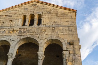 Antik bir Katolik kilisesinin ön cephesinde kemerler, desenler ve sütunlar sirrus bulutlu parlak mavi bir gökyüzüne karşı.