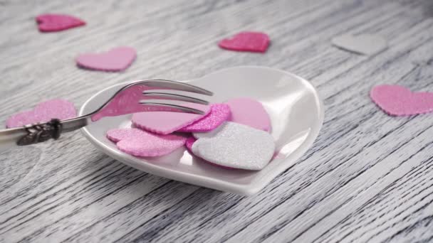 デザートフォークは 薄い質感の木製のテーブルの上に心臓の形で白いプレートにピンクと白の装飾的なバレンタインの束を攪拌します ハッピーバレンタインの日の挨拶 — ストック動画