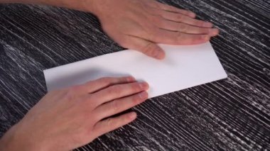 Genç bir adam, siyah desenli ahşap bir masa üzerinde beyaz bir ofis kağıdından origami uçağı yapıyor..