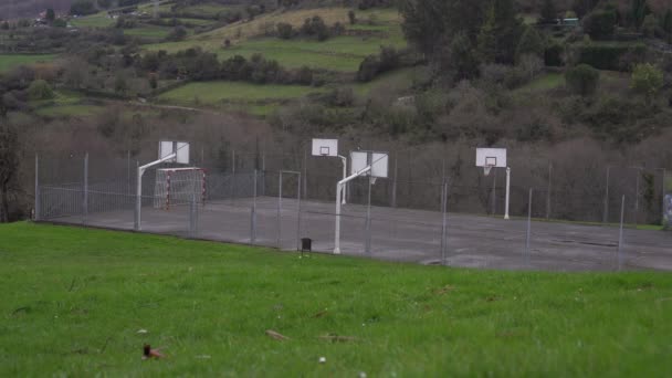 バスケットボールネットとリングとサッカーの目標を持つ山公園のスポーツフィールド 緑の植生や丘の中腹の木 ２つのカササギが建物に座って — ストック動画