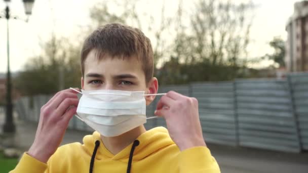 可悲的年轻人在金属栅栏的背景上戴上蓝色防护面具 在检测到头孢病毒时引入检疫和离开城市的限制的想法 — 图库视频影像