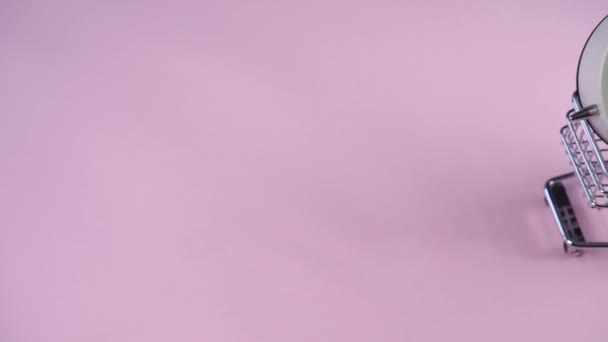 手卷一个装饰超市推车与白色闹钟里面粉红背景特写 — 图库视频影像