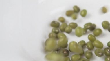 Yeşil fasulye düşer ve beyaz bir seramik tabağı doldurur. Ağır çekim. Makro