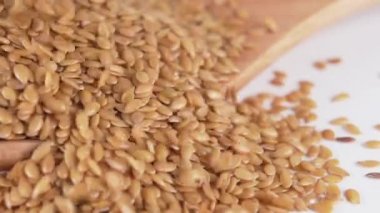 keten tohumu, ahşap bir kaşığa yığılıp yakın plan beyaz bir mutfak masasına düşer. Makro atış. Yavaş çekim.