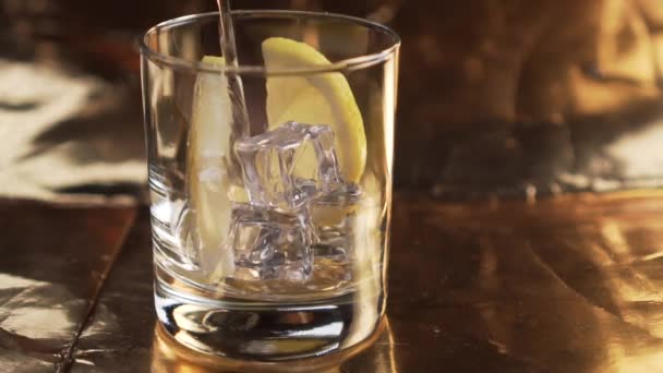 De l'eau gazeuse est versée dans un verre avec du citron et des glaçons. Bulles sur un fond texturé doré. Mouvement lent 