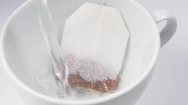 Verser de l'eau bouillante dans une tasse blanche avec un sac de thé rooibos additionné de fruits en gros plan sur une table de cuisine blanche. Plaisir du matin Tea Party 