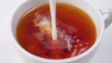 Süt beyaz fincanda siyah çaya dökülür. Kahvaltı ve enerji için sıcak aromalı içecek.