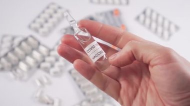 Coronavirus aşısı ampulü, beyaz bir masanın üzerindeki hapların ve kapsüllerin arka planında. Antiviral tedavi ve aşı