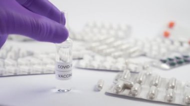 Coronavirus aşısı. Koruyucu eldivenli bir el, içinde ilaç ve tıbbi ekipman bulunan bir masadan cam ampul alıyor.