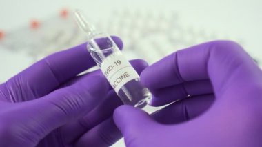 Coronavirus aşısı ampulü mavi koruyucu eldivenlerle tıbbi tabletler ve kapsüllerle beyaz bir masanın üzerinde. COVID-19 için uyuşturucu arama ve üretimi