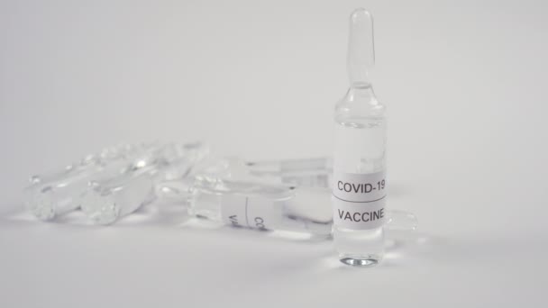 コロナウイルスワクチンとCovid 保護ブルーの手袋の手は 白いテーブルの上に薬とアンプルを設定します ウイルス感染症治療 — ストック動画