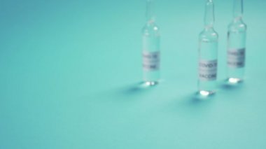 Coronavirus aşısı. Koruyucu tıp eldivenlerindeki bir el mavi bir yüzeye bulanık bir ampul yerleştirir. COVID-19 için ilaç.