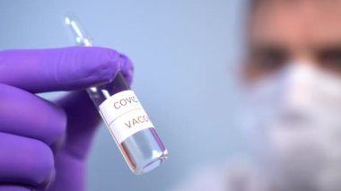 Coronavirus aşısı ampulü doktorun ellerinde maske ve koruyucu tıbbi eldivenler mavi arka planda. COVID-19 'dan yeni bir ilacın test ve kullanımı