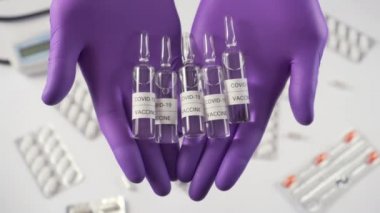 Coronavirus aşısı. Koruyucu eldivenlerdeki eller tıbbi ekipman ve kapsüllerle dolu bir masanın arka planında ilaç bulunan ampulleri gösteriyor. COVID-19 için ilaç.