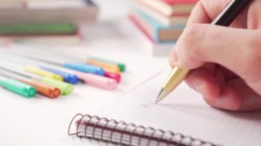 Yaratıcılık ve kitaplar için çok renkli okul gereçleri olan beyaz bir masadaki bir defterde siyah altın bir kalemle yazıyor. Coronavirus Karantina Mesafesi Öğrenme