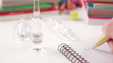COVID-19 ve kitaplardan aşı üreten ampullerle tıbbi bir iş yeri. Doktor bir deftere koronavirüs için yapılan testlerin sonuçlarını yazar. Yakın plan.