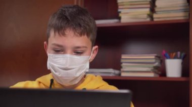Evde yüz maskeli bir dizüstü bilgisayarla genç yaşta öğreniyor. Okul malzemeleriyle dolu bir odada. Antiviral karantina sırasında internet üzerinden ödev yapmak