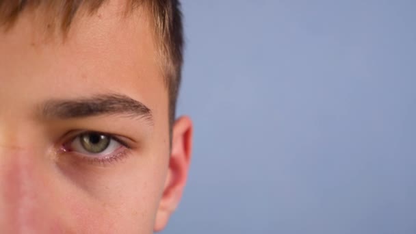 Adolescente Olha Com Olhos Tristes Pisca Metade Rosto Fundo Azul — Vídeo de Stock