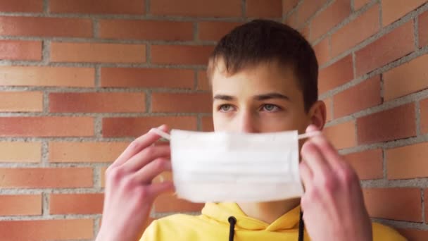 Mladý Muž Nasazuje Ochrannou Lékařskou Masku Cihlové Zdi Žluté Mikině — Stock video