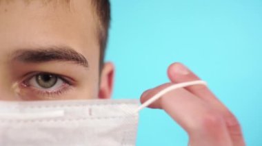 Tuğla duvarın yanında, tıbbi maske takmış, sarı kazaklı genç bir adam. Yakın plan portre. Sağlığı virüslerden ve alerjilerden koruma kavramı