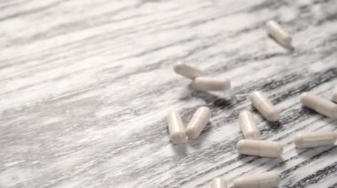 Beyaz tıbbi kapsüller ahşap, eski, siyah ve beyaz bir masa üzerine düşer. Covid-19 tedavi konsepti. Yakın plan. Yavaş çekim.