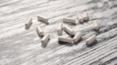 Beyaz tıbbi kapsüller ahşap, eski, yapısal siyah beyaz bir masa üzerine yığılır. Coronavirus tedavisi. Yakın plan. Ağır çekim. Tıbbi konsept