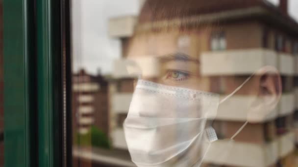 Jeune Homme Dans Masque Facial Quarantaine Regarde Tristement Par Fenêtre — Video