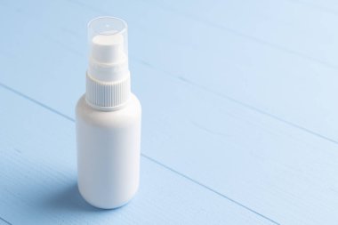 Mavi ahşap arka planda beyaz plastik bir kapta antiseptik sprey. Koronavirüsü önlemek için el dezenfeksiyonu. Kopyalama alanı.