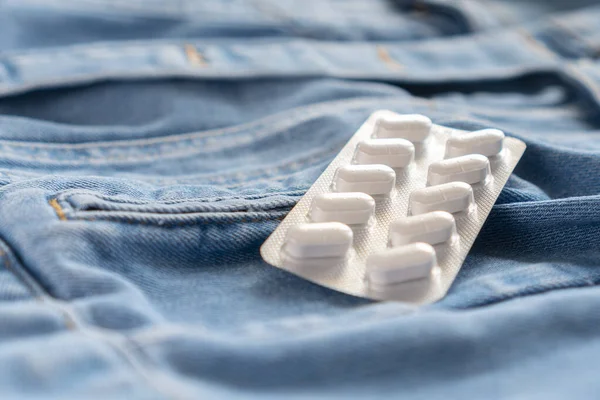 White pills in blister pack on blue jeans clothes pocket closeup. Coronavirus Symptom Treatment Concept. Copyspace. Abstract colorful background — Stock Image White Pills Blister Pack Blue Jeans Clothes Pocket Closeup Coronavirus Stock Picture