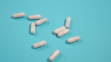 Beyaz tıbbi kapsüller mavi kağıt üzerine parlak bir yüzeye düşerler. Ağır çekimde yaklaşın. Virüs tedavisi kavramı