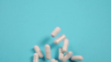 Beyaz tıbbi kapsüller fırlatılır ve mavi bir masanın üzerine düşer. Koronavirüs için antiviral ilaç araştırması ve testi. Tıbbi konsept