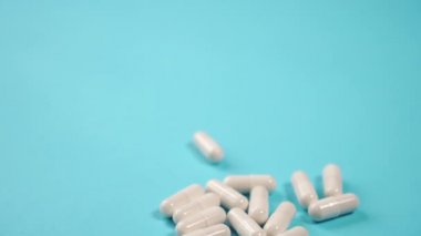 Mavi, parlak bir masa üzerinde beyaz tıbbi kapsüller. Kamerayı yavaşlat. Coronavirus tedavisi kavramı