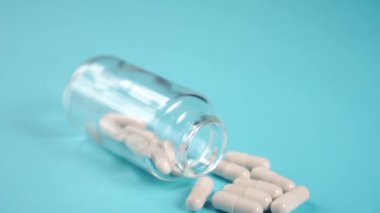 Cam ilaç şişesindeki tıbbi kapsüller mavi, parlak bir masada, yakın plan. Kamerayı yavaşlat. Coronavirus tedavisi kavramı