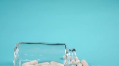 Mavi bir masanın üzerinde cam bir şişede tıbbi beyaz kapsüller. Kamerayı yavaşlat. COVID-19 'un önleme ve tedavi kavramı