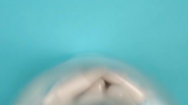 Yakın plan beyaz ilaç kapsülleri mavi parlak bir arka planda cam eczacılık konteynırında. Yukarıdan bak. Makro atış. Aşağıdan yukarıya doğru yavaş yol kamerası. Coronavirus aşısı konsepti