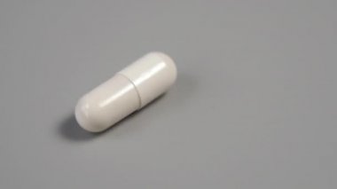 Yakından beyaz kapsül gri plastik bir yüzey üzerinde dönüyor. Ağır çekim. Makro atış. Tıbbi konsept. Coronavirus aşısı