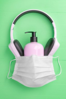Plastik pembe jel sabun kablosuz kulaklıkla kaplı açık yeşil ahşap arka planda tıbbi koruyucu maske. Soyutlama. Coronavirus konsepti evde kalır.