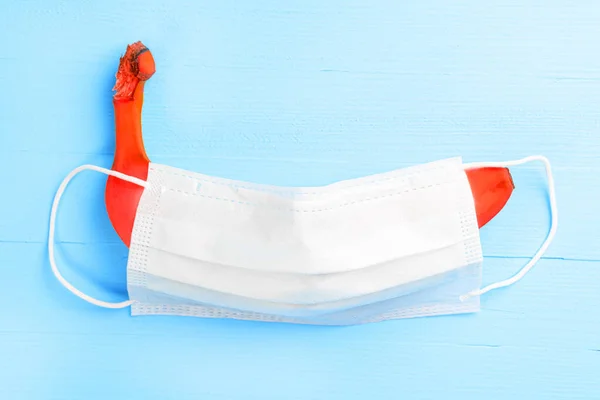 Ahşap açık mavi arka planda tıbbi koruyucu maskeyle kaplı kırmızı muz. Cinsel sorunlar ve cinsel yolla bulaşan enfeksiyonlar kavramı