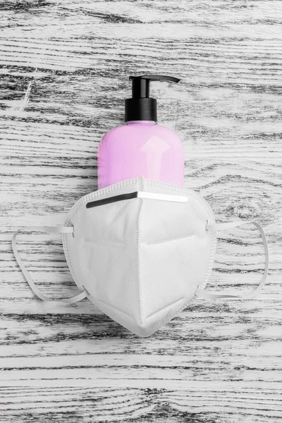 n95 respiratory mask covers a plastic container with pink mild soap and a black dispenser. On a black white wooden background close-up. Vertical view. Coronavirus and influenza prevention concept