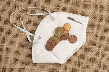 Çuval bezinin arka planında koruyucu bir tıbbi maskede bulunan paralar. Bir sürü para. Coronavirüs salgınından sonraki ekonomik kriz kavramı.