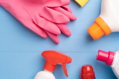 Parlak plastik şişelerde deterjan seti ve ahşap mavi arka planda ev ödevi için pembe koruyucu eldivenli sarı bir bez. Kopyalama alanı