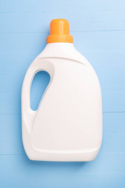Ahşap açık mavi arka planda yıkanmak için deterjanı olan parlak turuncu kapaklı beyaz plastik bir şişe. Kopyalama. Harekete geç.