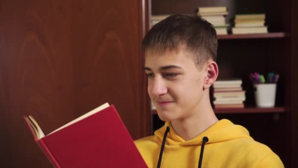 家里的年轻学生在书架上看一本书 书架上有课本 穿着一件黄色的汗衫特写 网上远程学习 — 图库视频影像