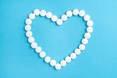 Mavi kâğıt üzerinde beyaz tıbbi haplardan yapılmış kalp şekli. Fikir Kardiyo tedavisi. İlaç, eczane ve sağlık kavramı.