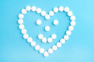 Gülümseyen kalp şeklinde gülücük mavi kağıtta beyaz tıbbi haplardan yapılmış. Sağlık ve bakım kavramı