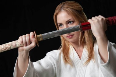 Sarışın, güzel bir kız Katana kılıcını iki eliyle siyah arka planda tutuyor. İzole edilmiş resim