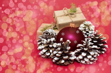 Kırmızı top ve köknar kozalaklı Noel ya da yeni yıl kompozisyonu. Kırmızı arka planda yeşil dallı hediye kutuları renkli bokeh.